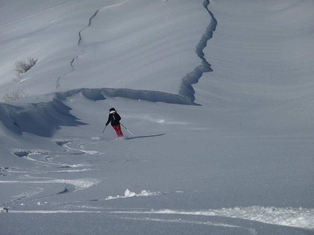 Laure vue de dos fait la première trace à skis dans la neige poudreuse de la pistes des Lanches.